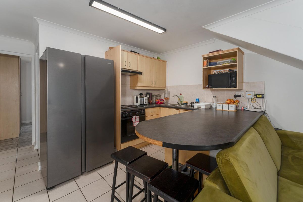 Compact kitchen featuring light wood cabinetry, laminate countertops, a breakfast bar, and tiled flooring, providing a functional workspace within the apartment.