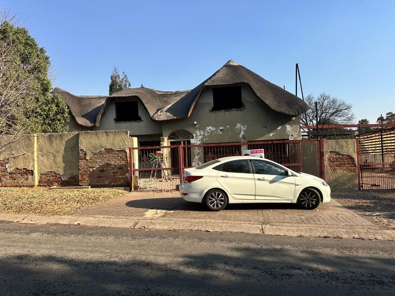 Front elevation of a house featuring a thatch roof, perimeter wall, and gated entrance, currently showing significant signs of exterior wear and maintenance requirements.