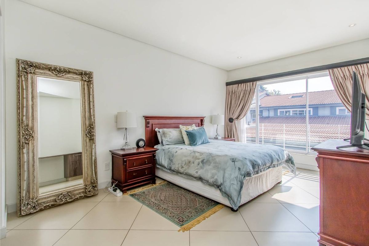 A bright and spacious bedroom featuring large windows with curtain tracks, tiled flooring, and recessed ceiling lighting.