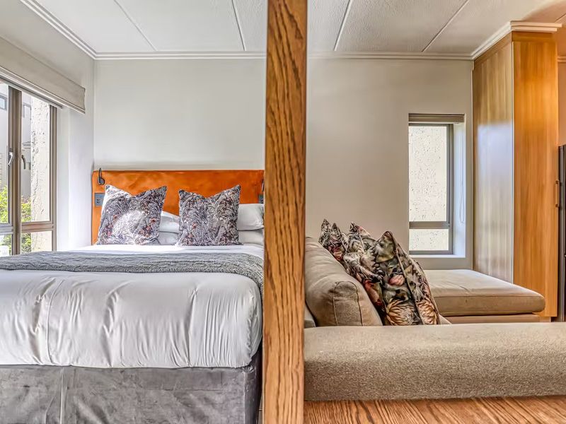 A well-lit open-plan living and sleeping area featuring modern built-in cabinetry, large windows, and a functional timber room divider.