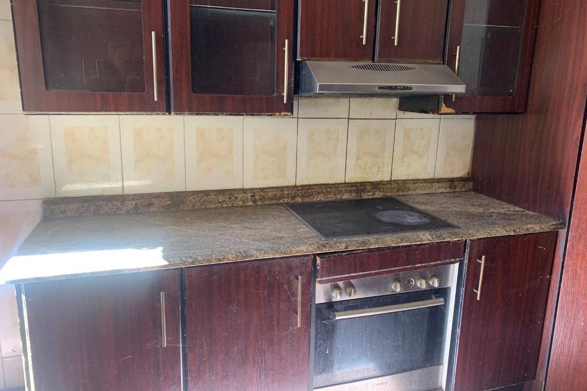 A dated kitchen area featuring dark wood-look cabinetry, a stone-effect countertop, built-in oven, and extractor fan with a tiled backsplash.