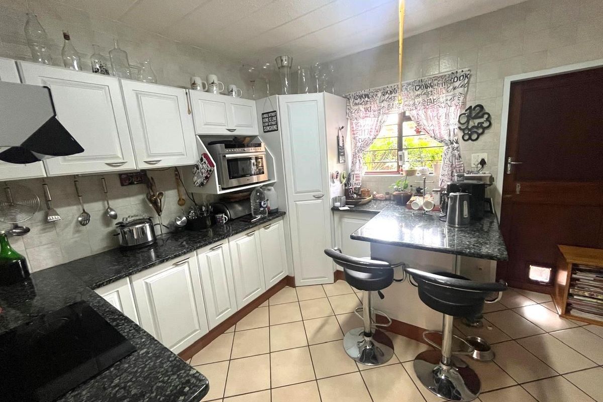 A functional kitchen featuring white cabinetry, dark granite countertops, a breakfast nook, and tiled flooring with direct access to the exterior.