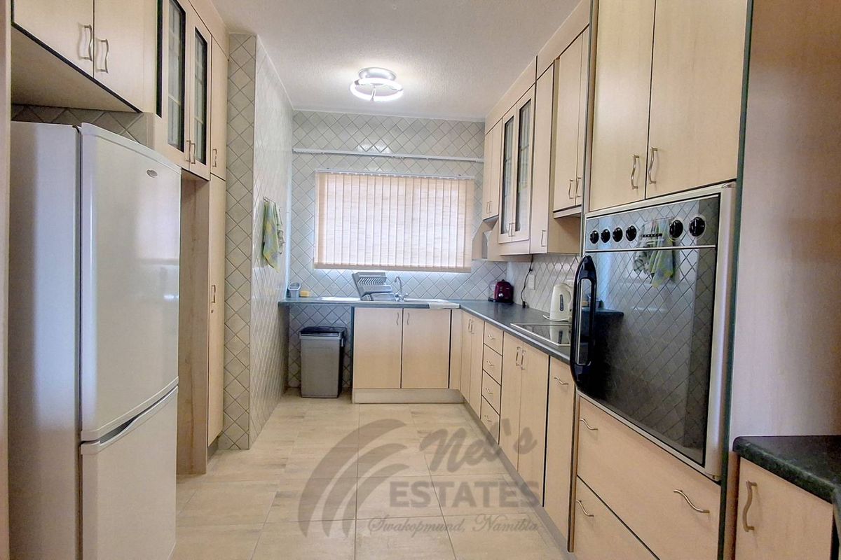 A functional kitchen featuring light wood-toned cabinetry, tiled splashbacks, a built-in oven, and ample counter space with a window for natural light.
