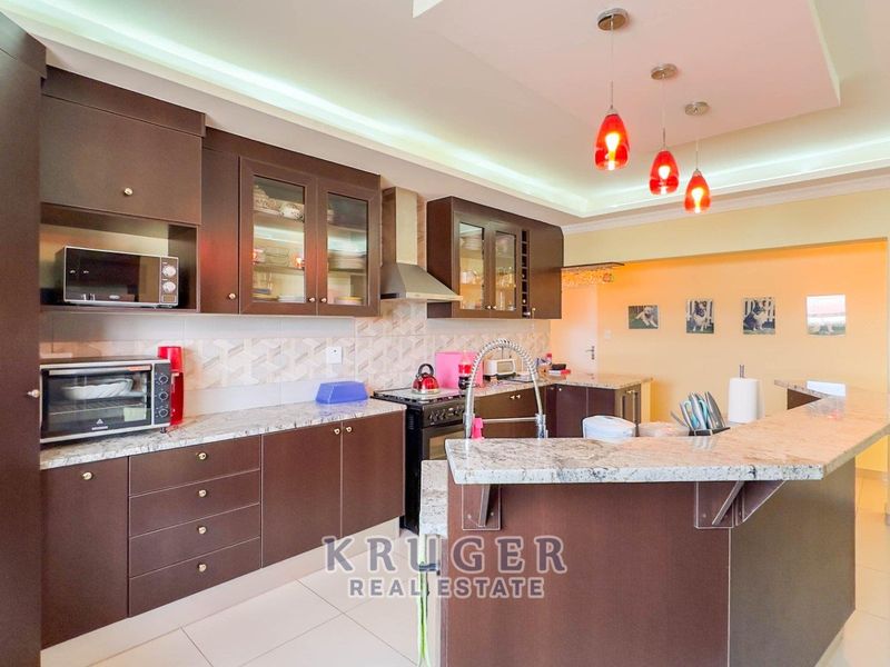 Modern kitchen featuring dark wood cabinetry, granite countertops, a tiled backsplash, and a breakfast bar island with pendant lighting.