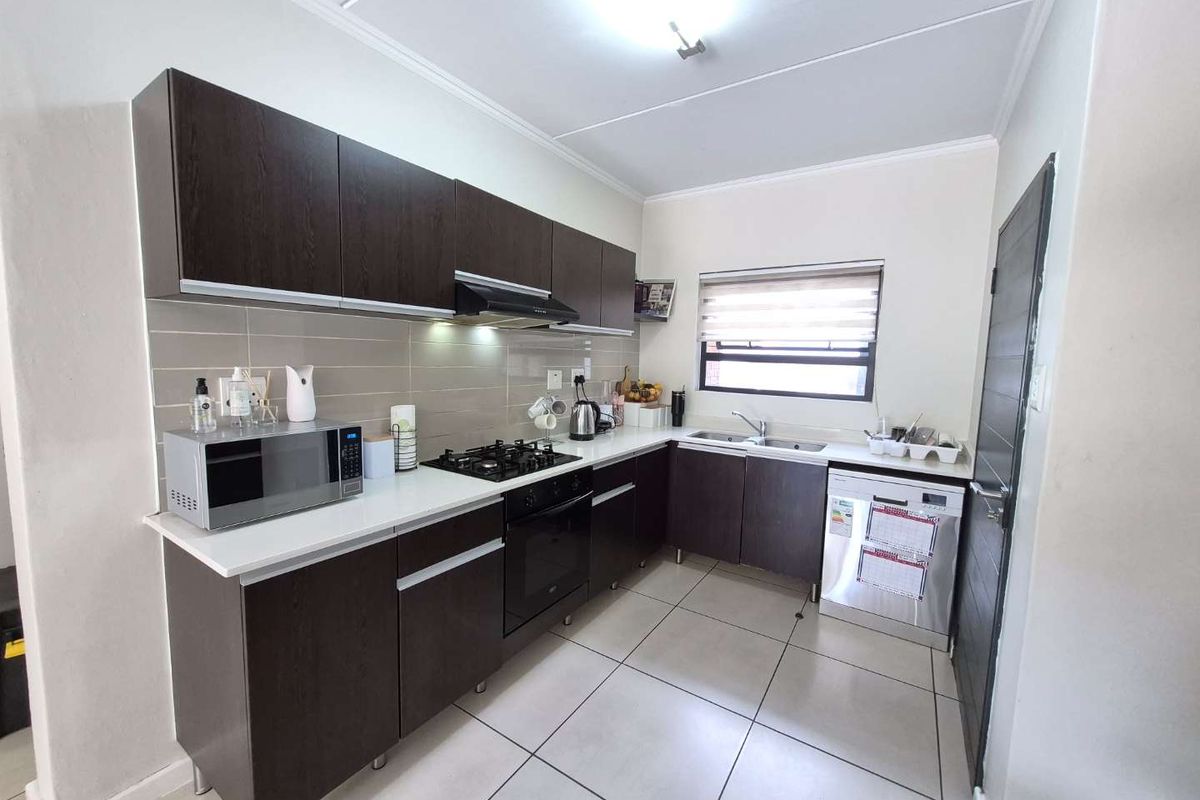 A functional kitchen featuring dark wood cabinetry, light countertops, a built-in oven, gas hob, extractor fan, and tiled flooring.