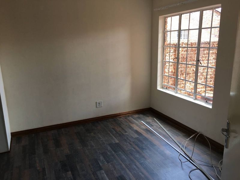 An empty bedroom featuring dark laminate flooring, timber skirting boards, and a steel-framed window overlooking an exterior brick wall.
