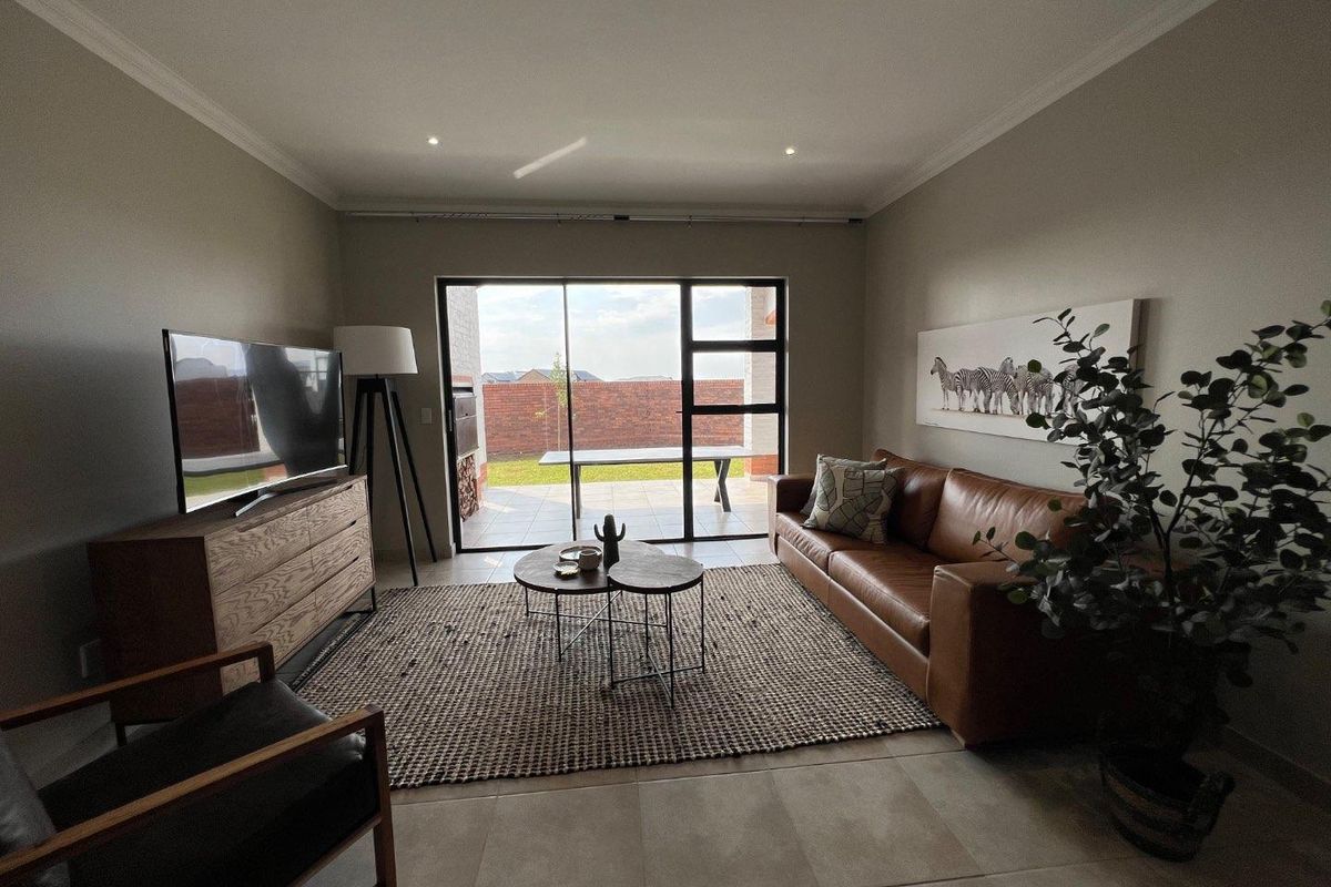 A well-lit living room featuring large sliding glass doors that open onto a paved patio and garden area.