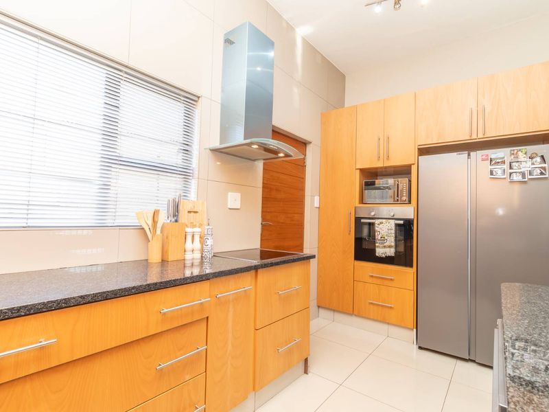 Modern kitchen featuring light wood cabinetry, granite countertops, stainless steel appliances, and tiled flooring with ample natural light.