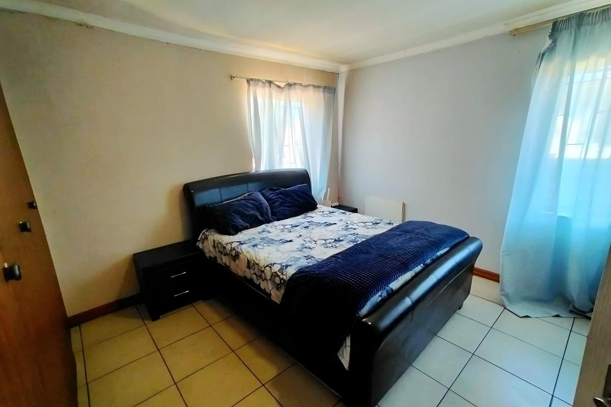 A functional bedroom featuring tiled flooring, neutral wall finishes, and dual windows allowing for natural light.