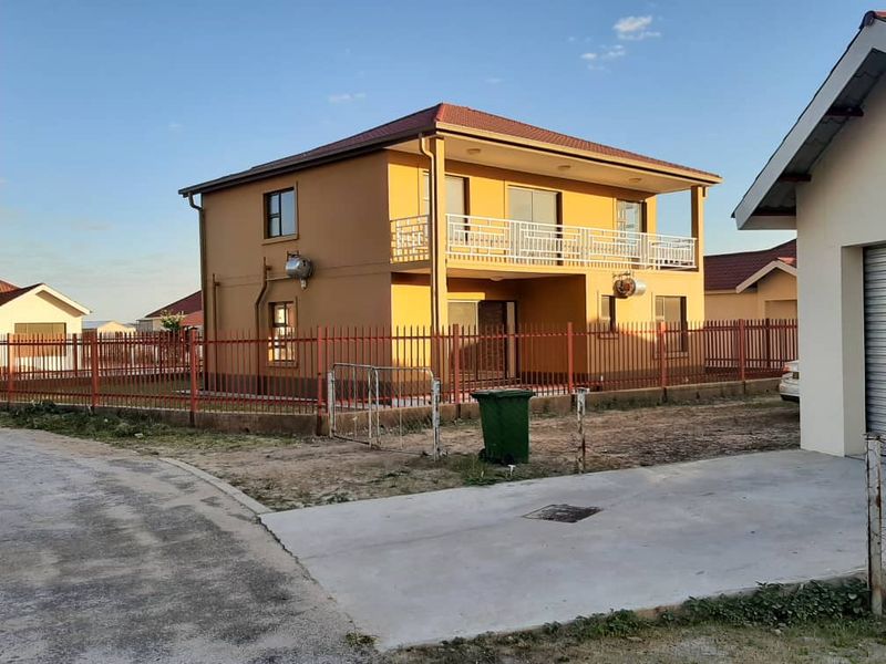 A two-story residential house featuring a balcony with metal railings, a tiled roof, and a fenced yard with a concrete driveway.