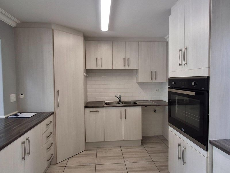 A clean, modern kitchen featuring light wood-grain cabinetry, dark laminate countertops, a built-in oven, and a classic subway tile backsplash.