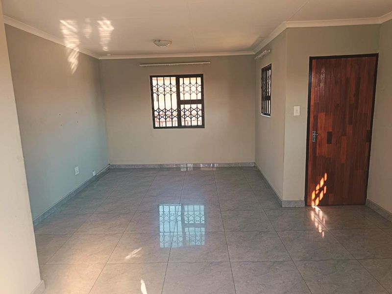 A bright, empty living area featuring neutral wall tones, large format floor tiles, and secure window bars.
