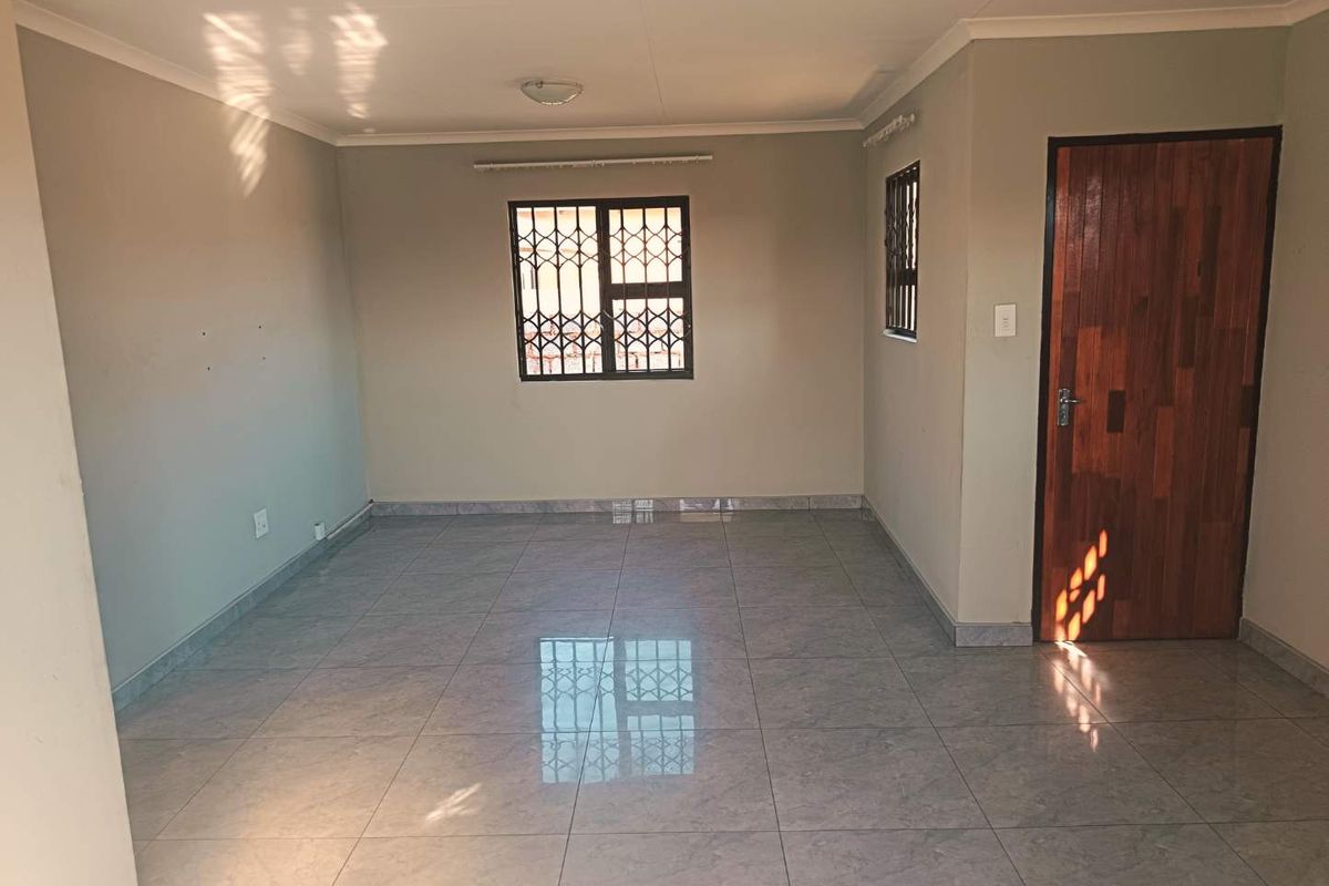 A bright, empty living area featuring neutral wall tones, large format floor tiles, and secure window bars.