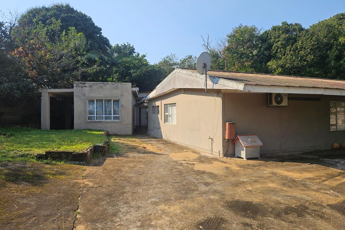 Rear view of the property featuring a concrete driveway, brick exterior walls, and a corrugated metal roof with an installed air conditioning unit.