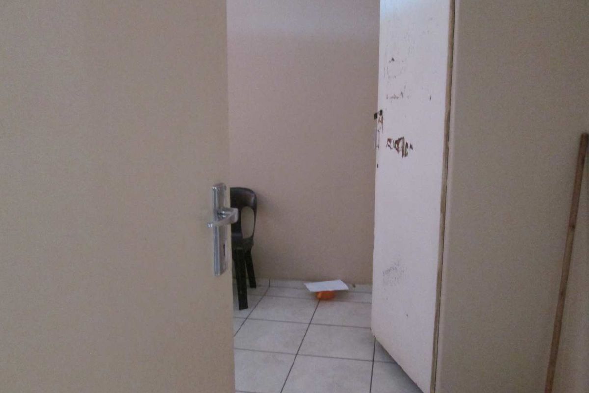 A small, sparsely furnished bedroom featuring tiled flooring and a built-in cupboard with visible wear on the door finish.
