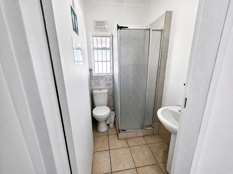 A compact bathroom featuring a shower enclosure, pedestal basin, and toilet with tiled flooring and natural light from a window.