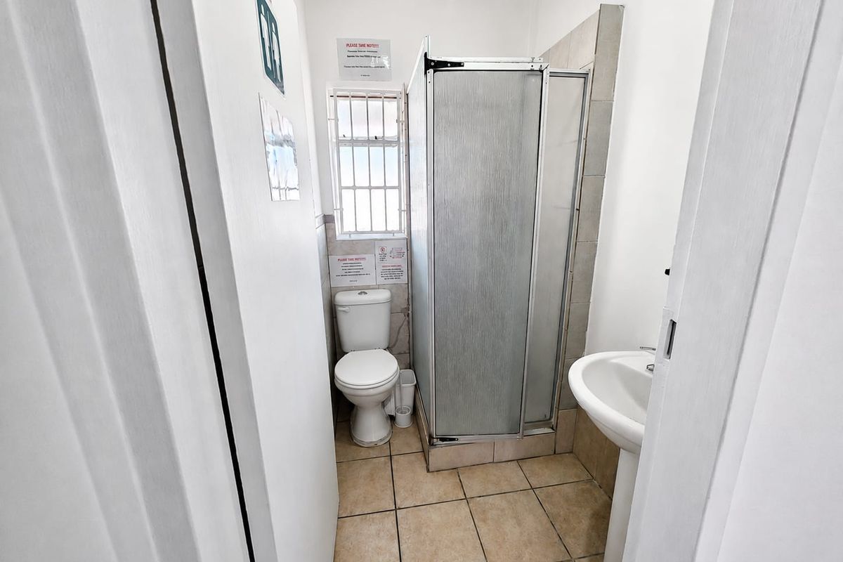 A compact bathroom featuring a shower enclosure, pedestal basin, and toilet with tiled flooring and natural light from a window.