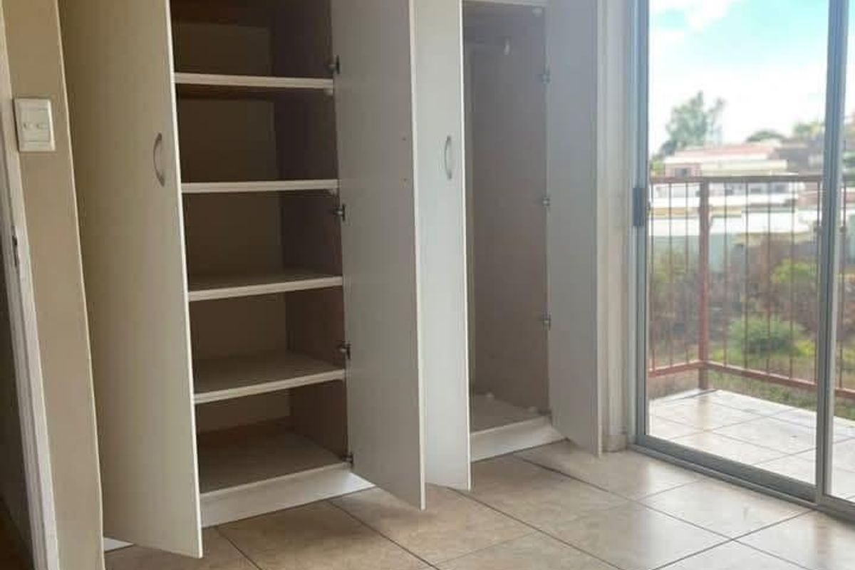 A bright, empty bedroom featuring built-in cupboards, tiled flooring, and a sliding glass door leading to a private balcony.