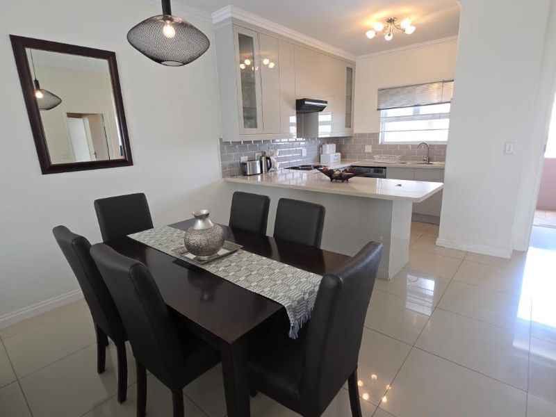 Modern open-plan kitchen and dining area featuring glossy cabinetry, stone countertops, subway tile backsplash, and polished porcelain floor tiles.