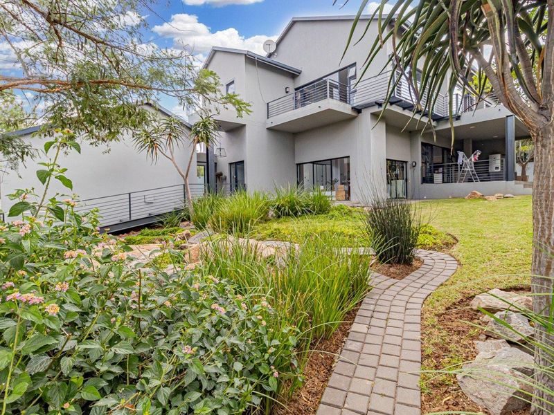Rear view of a modern multi-level house featuring a landscaped garden, paved walkway, and spacious balconies with metal railings.