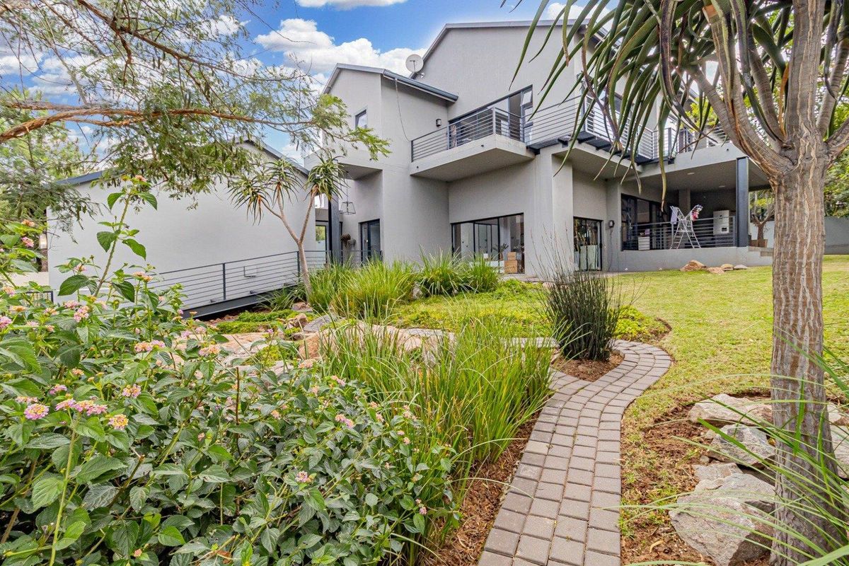 Rear view of a modern multi-level house featuring a landscaped garden, paved walkway, and spacious balconies with metal railings.