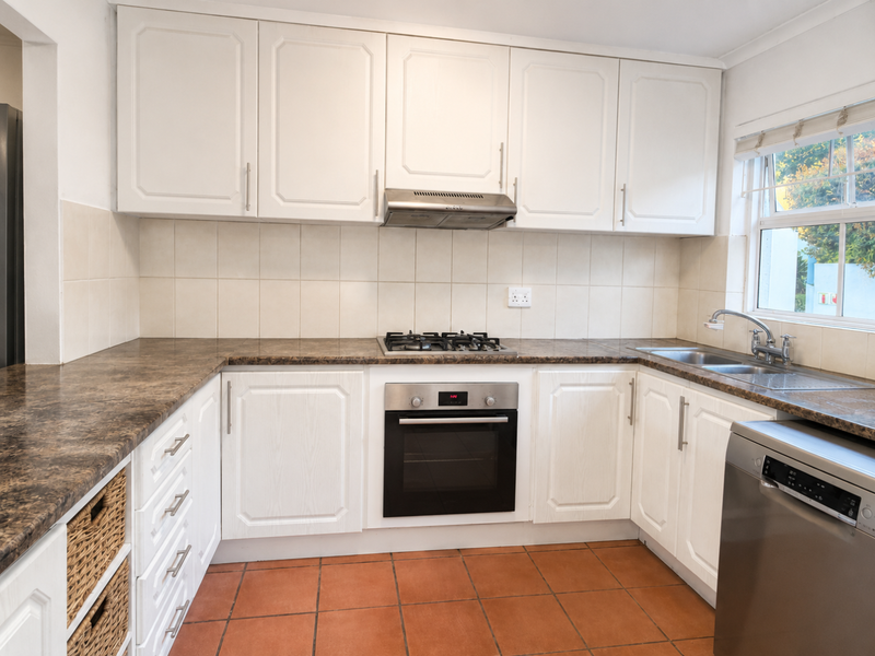 A functional kitchen featuring white cabinetry, laminate countertops, a gas hob, built-in oven, and terracotta floor tiles, offering a clean and practical workspace.
