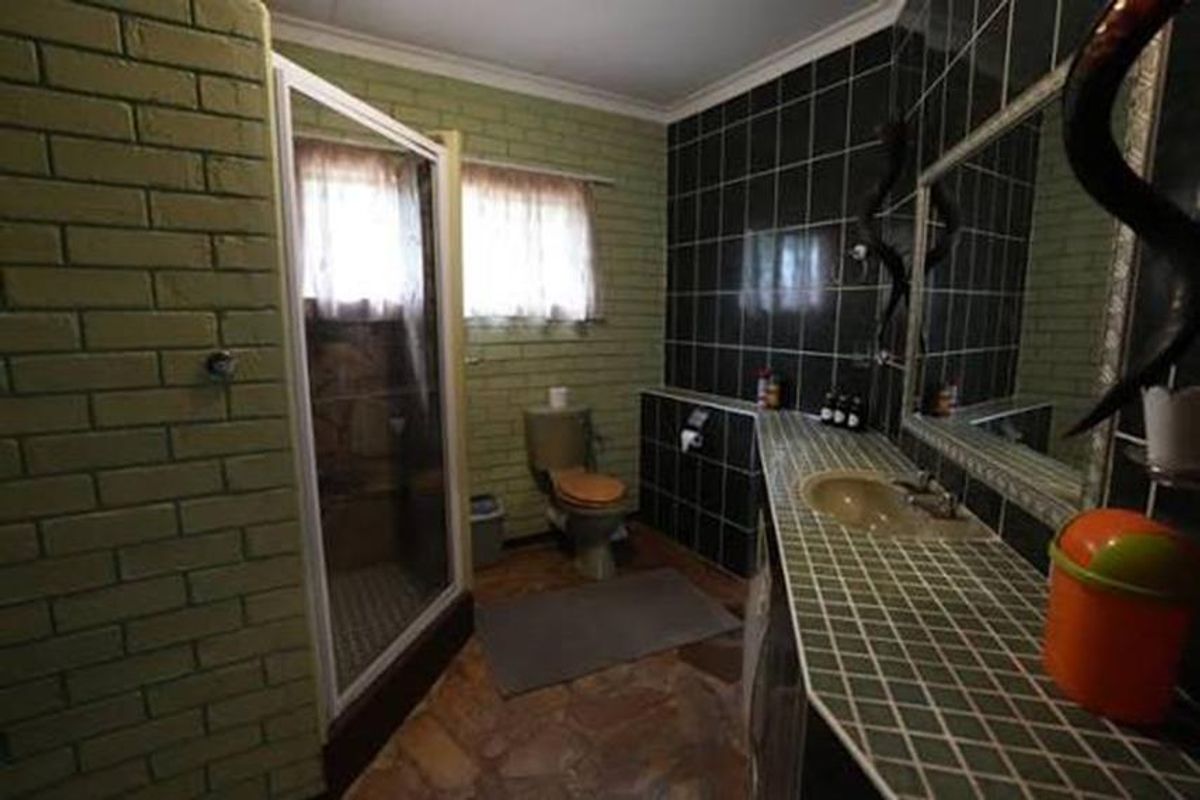 A functional bathroom featuring a shower enclosure, toilet, and a tiled vanity basin with a large wall mirror.