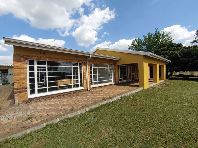 Rear view of the house featuring a spacious paved patio, covered veranda, and large windows with security bars overlooking the garden.