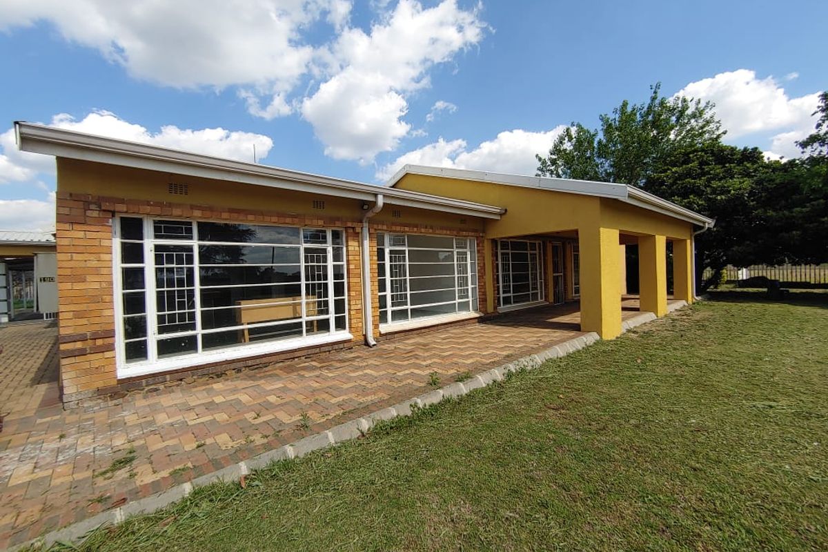 Rear view of the house featuring a spacious paved patio, covered veranda, and large windows with security bars overlooking the garden.