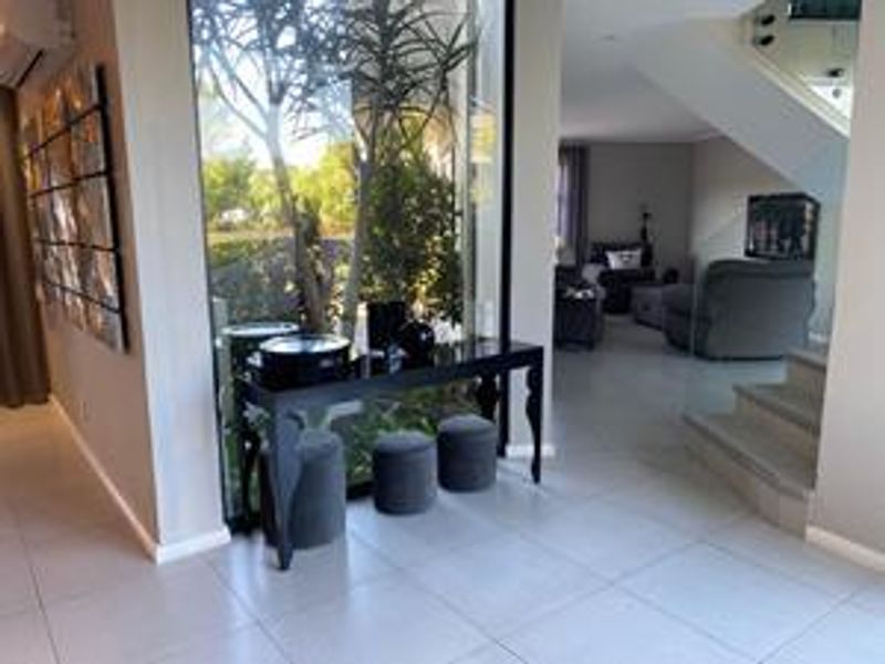 Modern entrance hall featuring large floor-to-ceiling windows, tiled flooring, and a glass-balustrade staircase leading to the upper level.