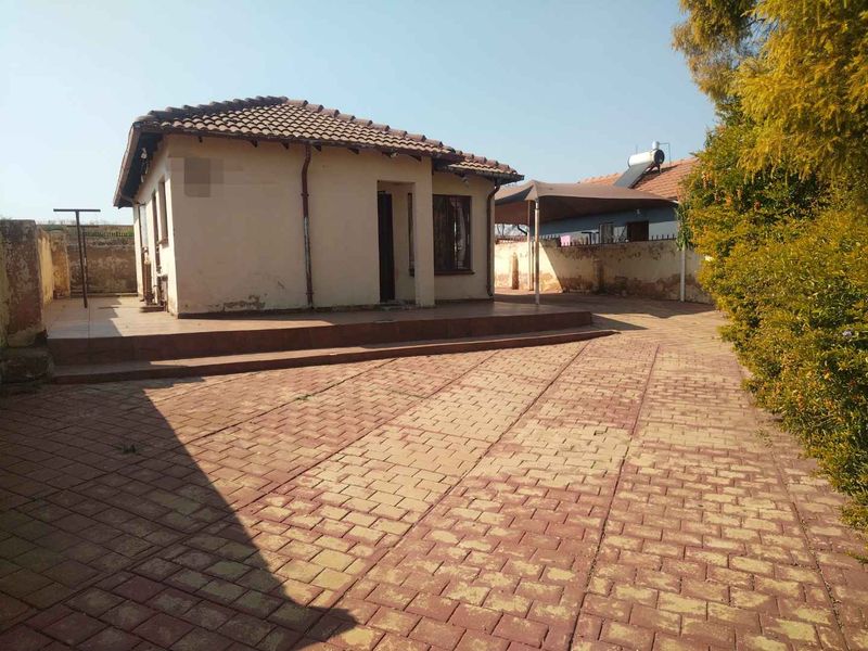 Rear view of the property featuring a paved courtyard, raised patio area, and a detached structure with a tiled roof.