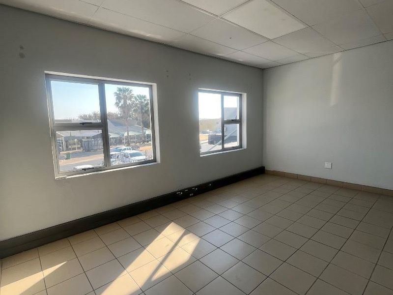 An empty office space featuring tiled flooring, a suspended ceiling, and large windows providing natural light.
