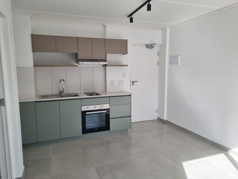 Modern open-plan kitchen featuring sage green lower cabinetry, neutral upper cabinets, integrated oven, hob, and extractor fan with sleek tiled flooring.