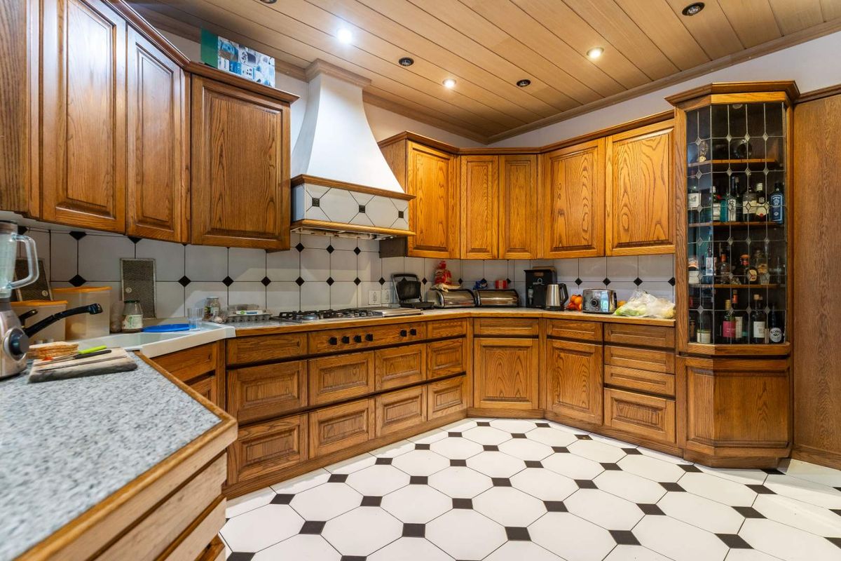 A traditional kitchen featuring solid wood cabinetry, a built-in extractor hood, granite-style countertops, and classic black and white checkered floor tiling.