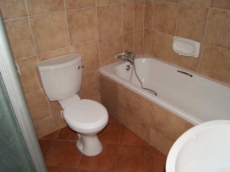A functional bathroom featuring ceramic wall and floor tiles, a built-in bathtub, a toilet, and a basin.