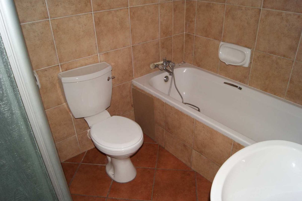 A functional bathroom featuring ceramic wall and floor tiles, a built-in bathtub, a toilet, and a basin.
