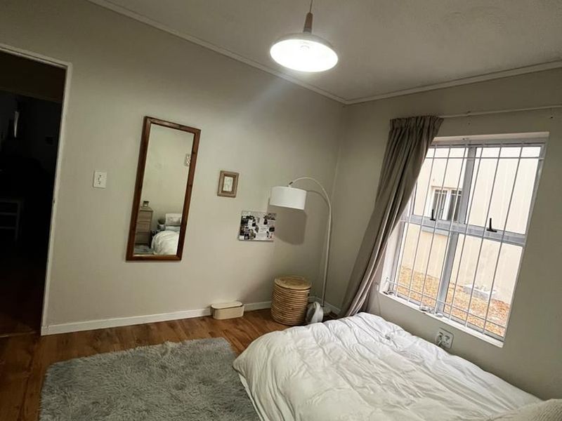 A bedroom featuring laminate flooring, a window with security bars, and a central pendant light fixture.