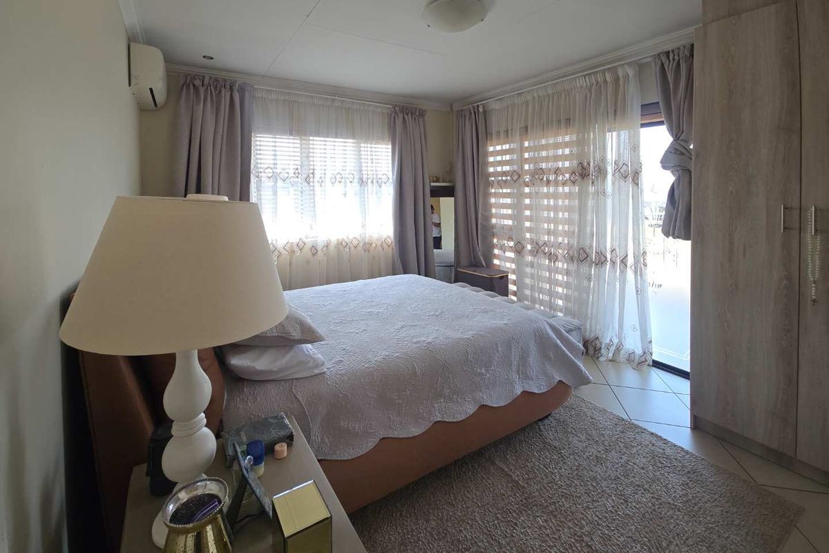 A well-lit bedroom featuring tiled flooring, a built-in wardrobe, an air conditioning unit, and sliding glass doors providing access to the exterior.