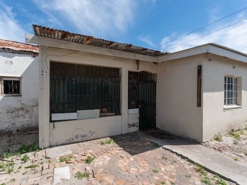 Front exterior view of a house featuring a corrugated metal roof, security bars, and a brick-paved courtyard area in need of maintenance.