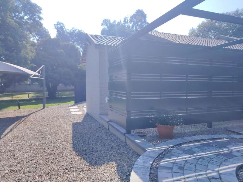 Rear exterior view of the property featuring a paved patio area, modern slatted privacy screen, and gravel landscaping under a shade sail structure.