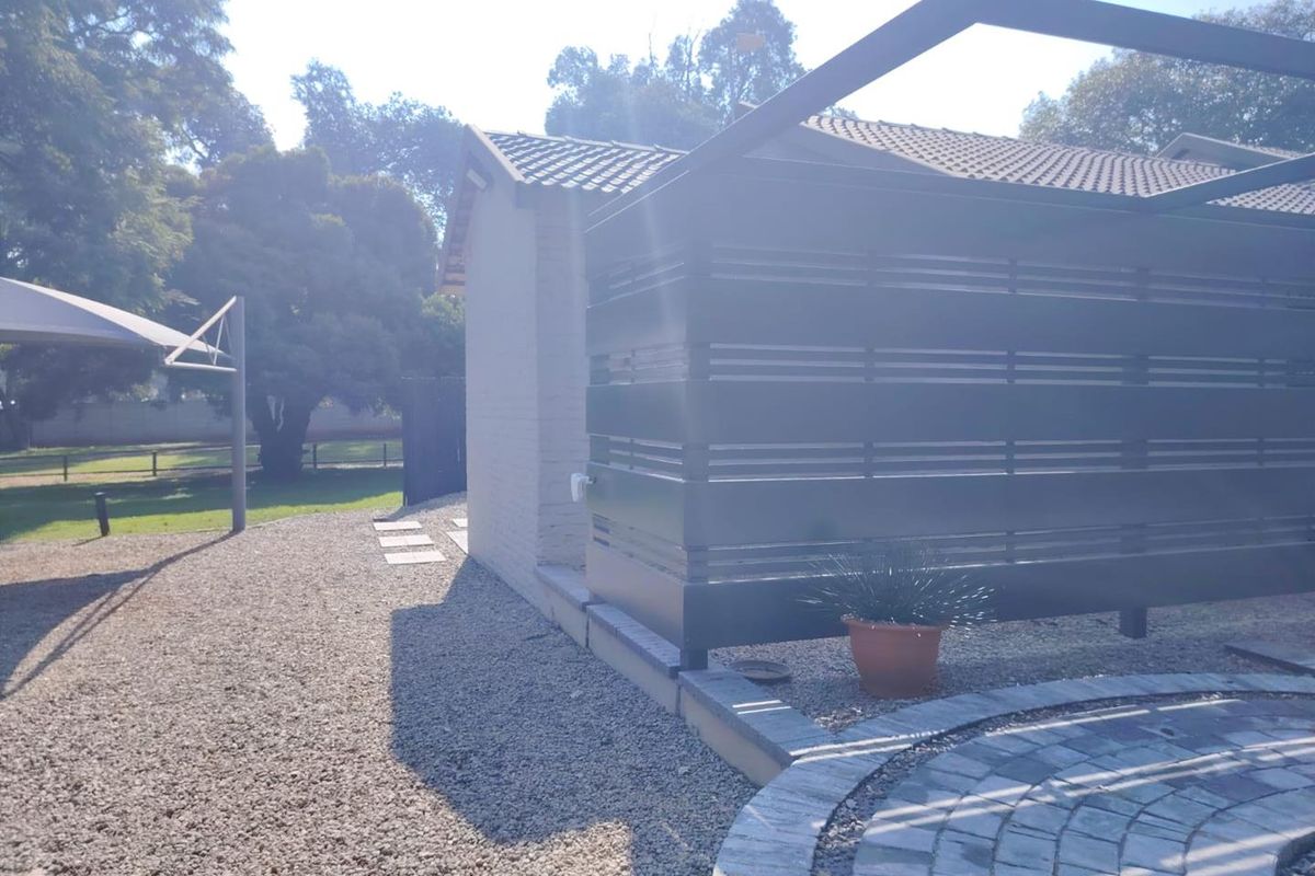 Rear exterior view of the property featuring a paved patio area, modern slatted privacy screen, and gravel landscaping under a shade sail structure.