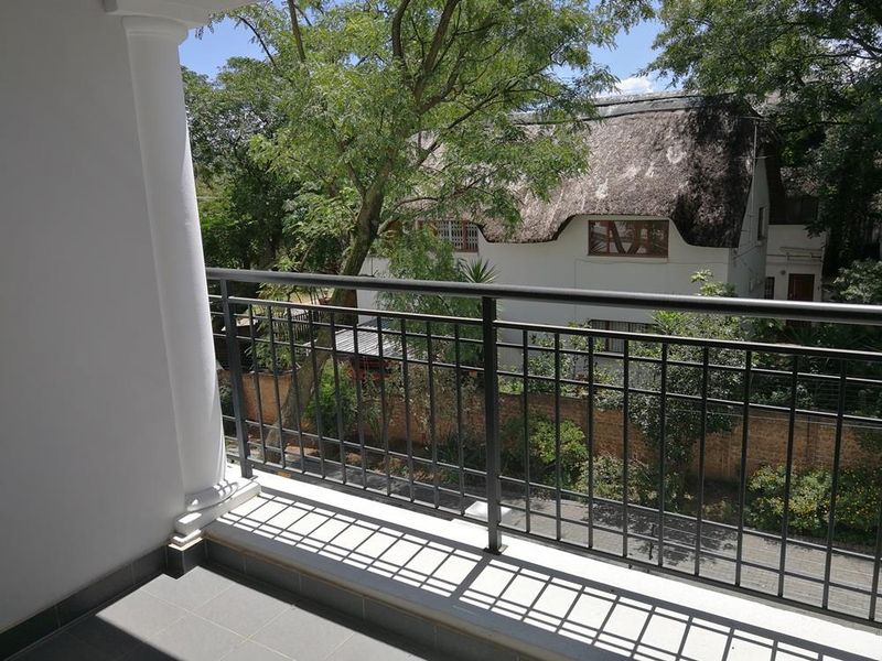 A clean, private balcony featuring tiled flooring and a secure metal balustrade, offering a pleasant view of the surrounding greenery and neighboring properties.