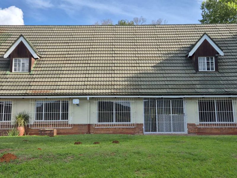 Rear view of a two-story house featuring a tiled roof with dormer windows, security bars on windows, and a spacious lawn area.