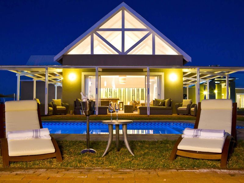 A beautifully illuminated evening view of a swimming pool and covered patio area, featuring a striking timber-framed gable roof structure.