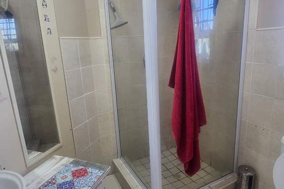 A functional bathroom featuring a corner shower enclosure, tiled flooring, wall-mounted mirror, and standard sanitary fixtures.