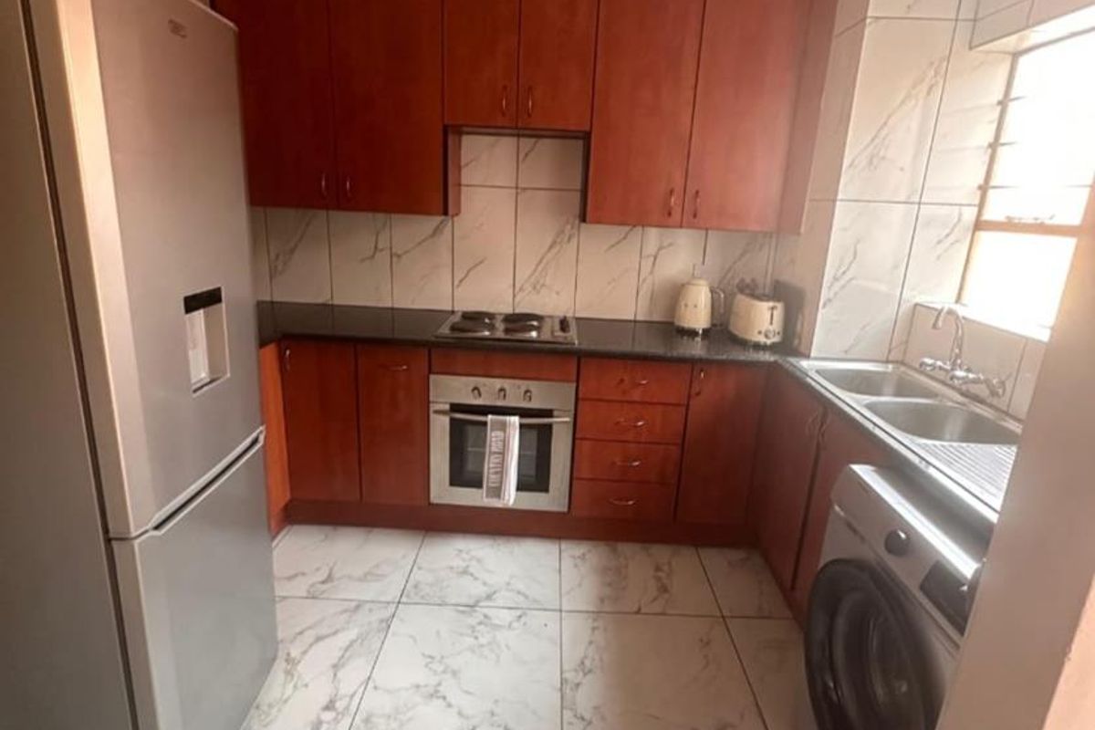 A compact kitchen featuring cherry-wood cabinetry, marble-look floor tiles, a built-in oven and hob, and a double-basin sink with integrated laundry plumbing.