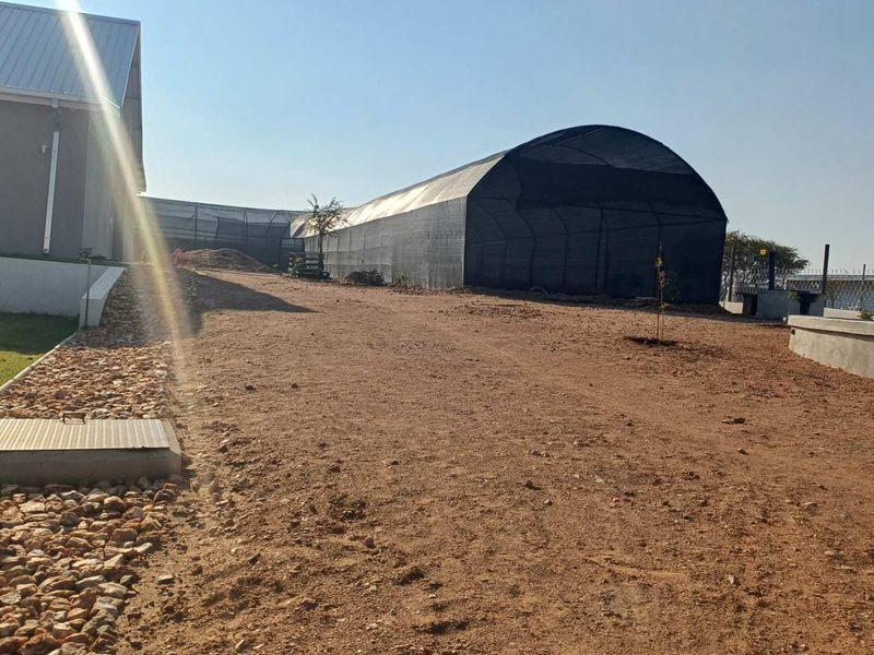Rear exterior view showing a large shade cloth tunnel structure, unpaved ground, and basic site infrastructure.