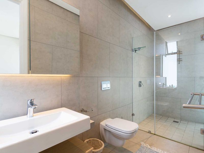 Modern bathroom featuring a floating vanity, wall-mounted toilet, and a spacious walk-in glass shower with contemporary neutral tiling.