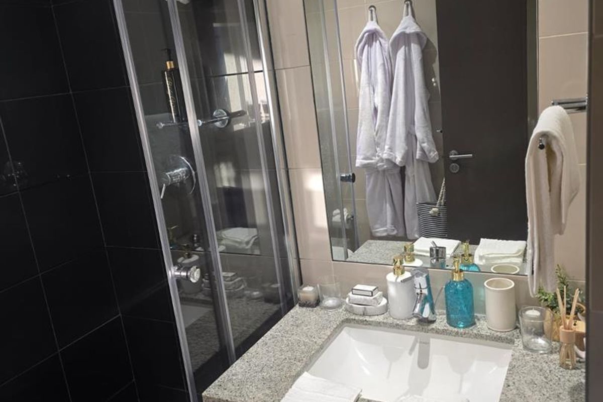 Modern bathroom featuring a granite vanity top with an integrated sink, a glass-enclosed shower with black tiling, and a large wall-mounted mirror.