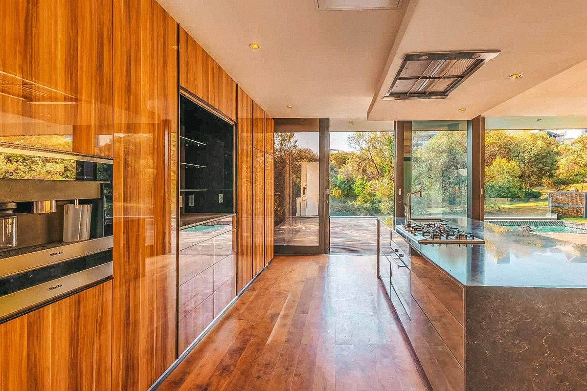 Modern kitchen featuring high-end wood cabinetry, integrated Miele appliances, a large stone island with a gas cooktop, and floor-to-ceiling glass doors opening to the garden.